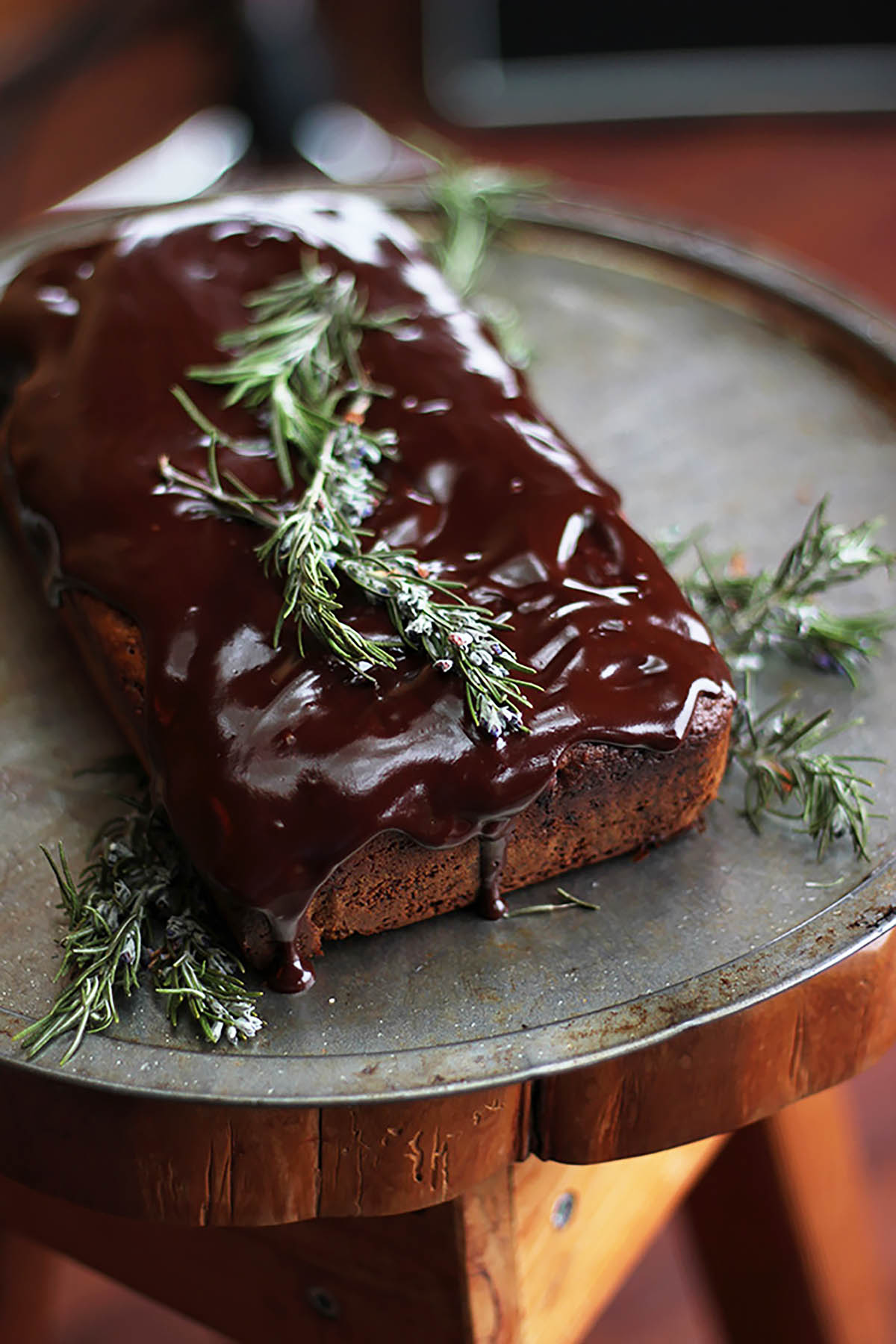 A chocolate loaf cake topped with shiny ganache and rosemary.
