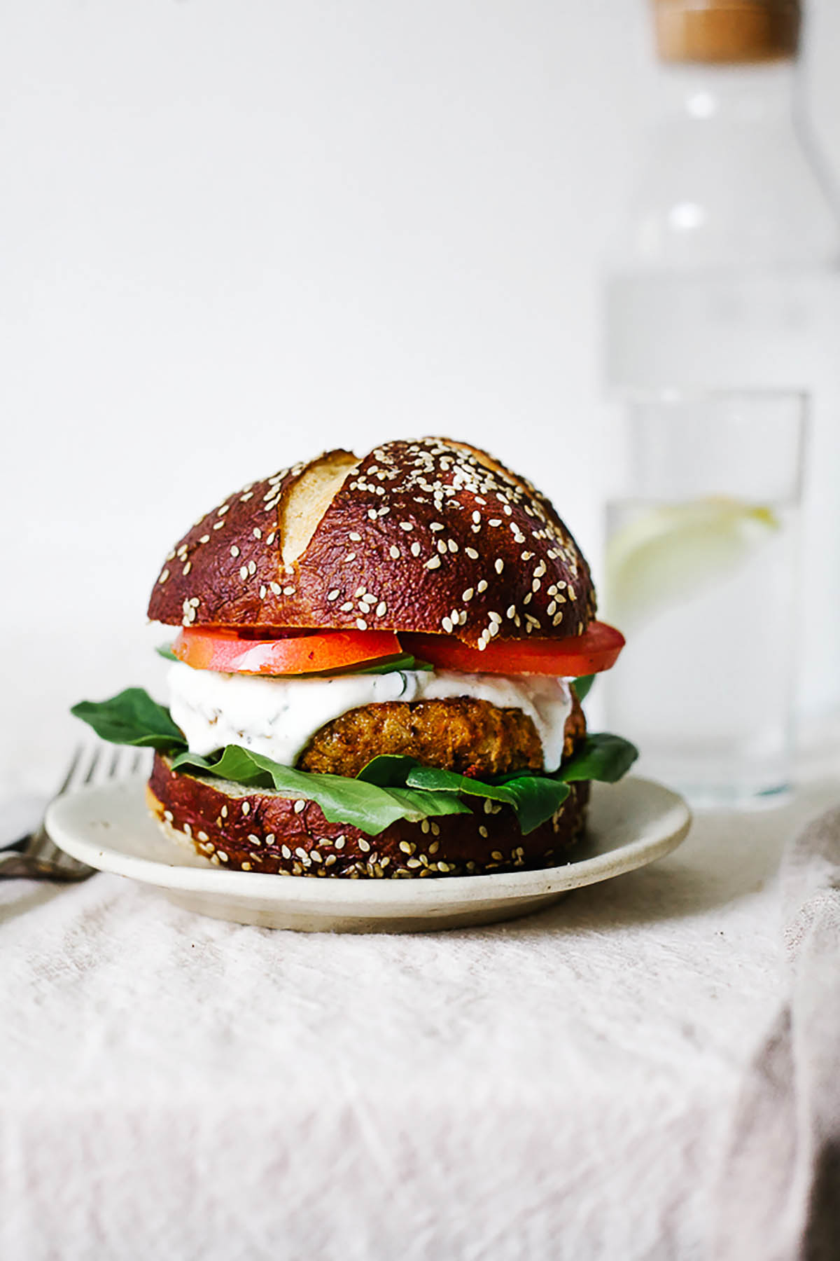 A chickpea burger on a bun topped with lettuce, white sauce, and tomatoes.