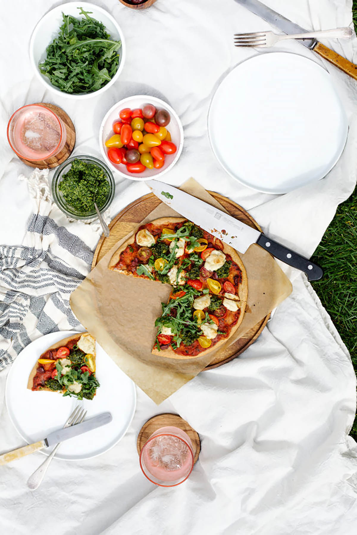 A small pizza in a picnic setting with a slice cut.