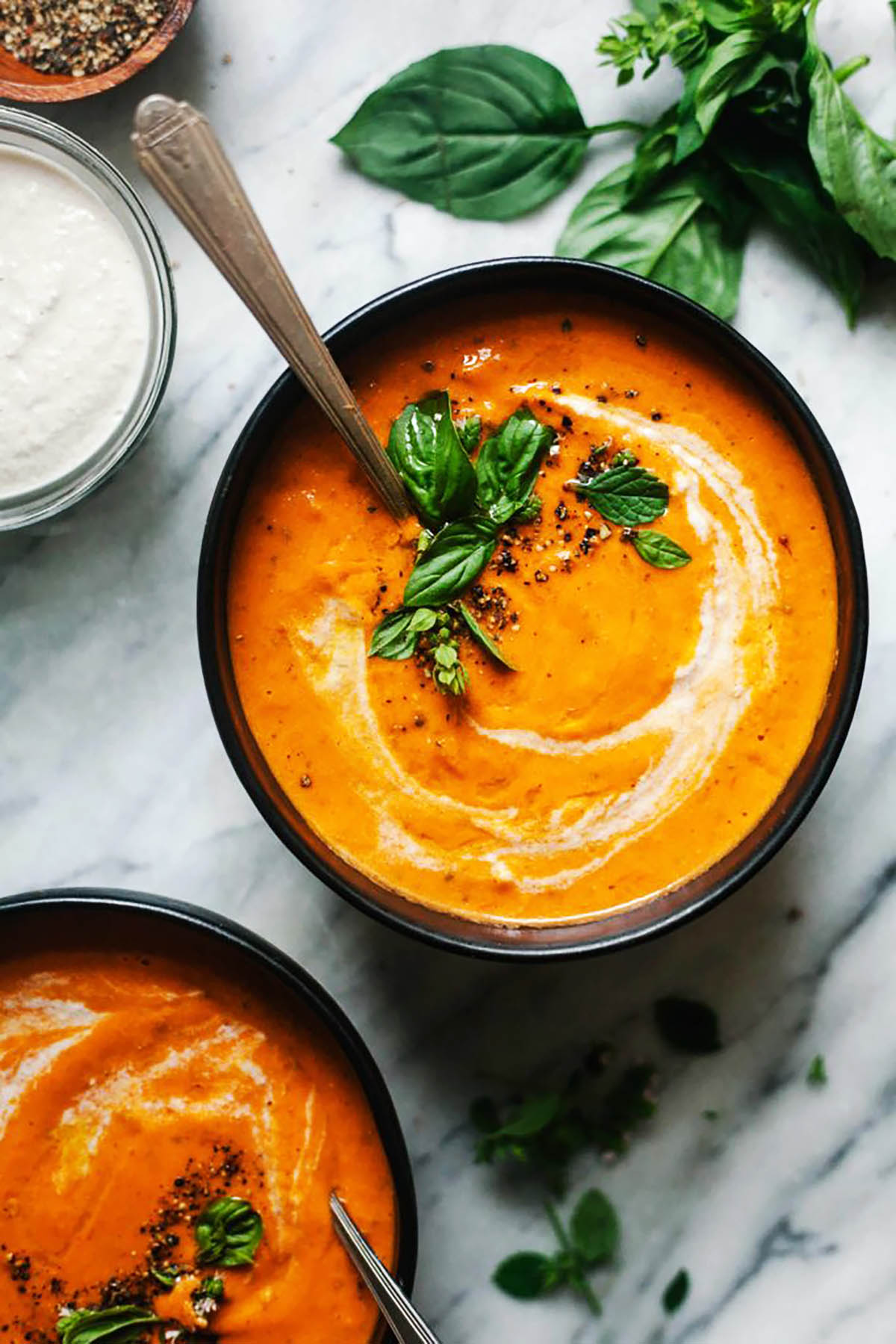 Tomato soup in bowls topped with cream and herbs.