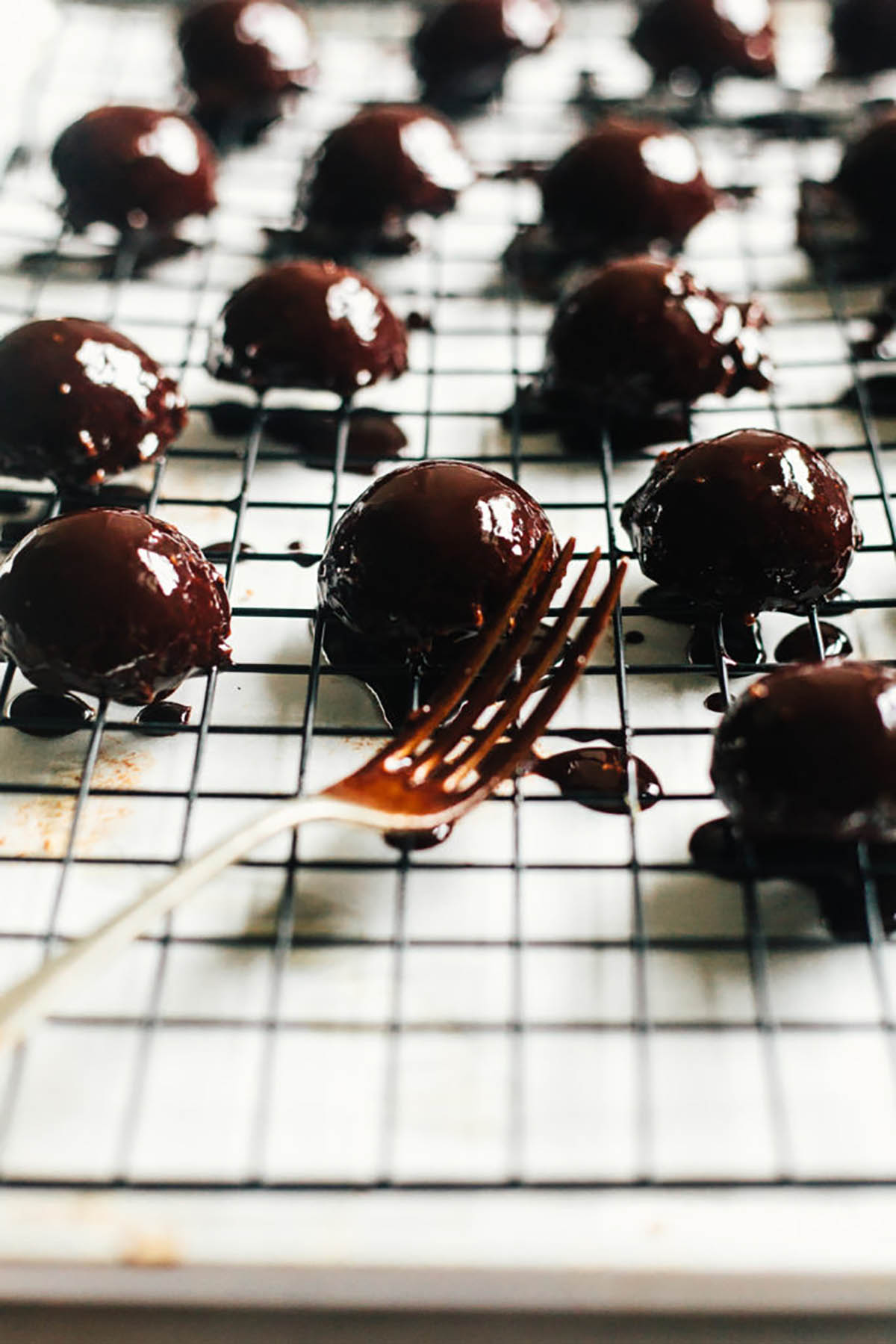 Several round treats covered in melted chocolate on a wire rack.