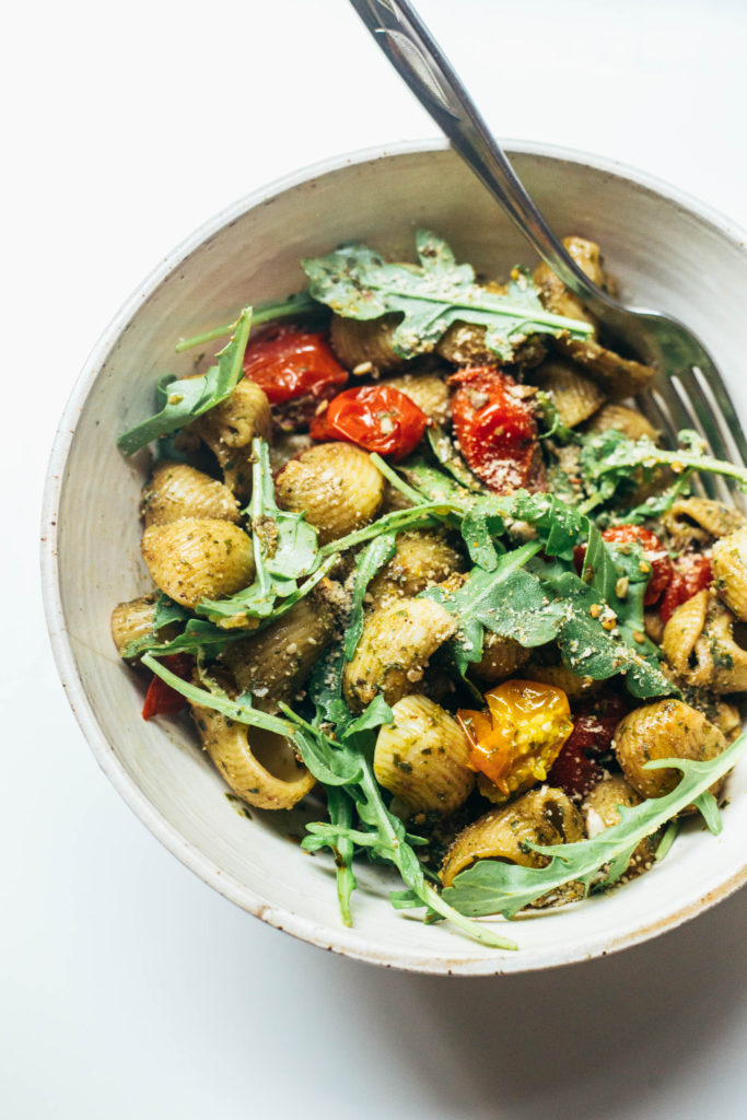 Simple summer pasta with arugula pesto, crunchy sunflower seeds, and golden roasted tomatoes. Dinner in under 30