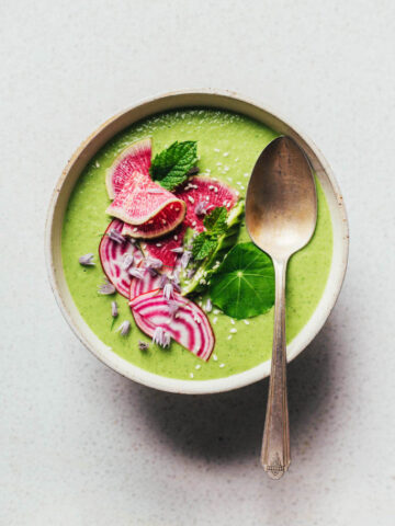 Green soup in a bowl topped with radish, herbs, and a spoon.