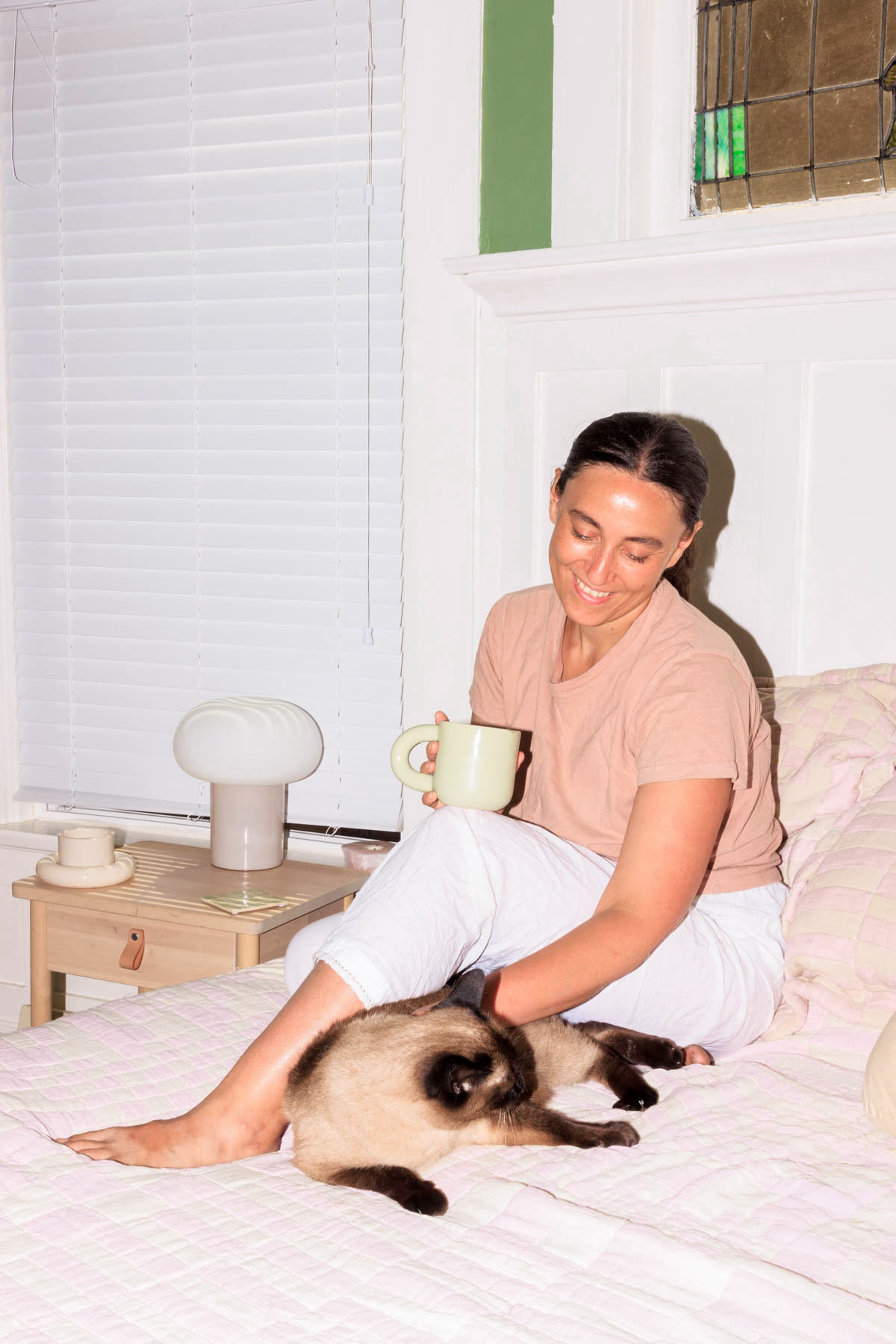A woman sitting on a bed with a small cat.