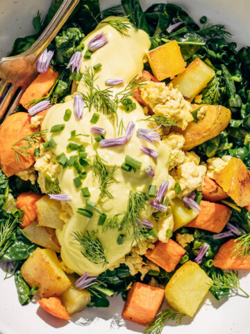 Close up of golden vegan hollandaise made with cashews on a breakfast bowl with herbs, scramble, and yams