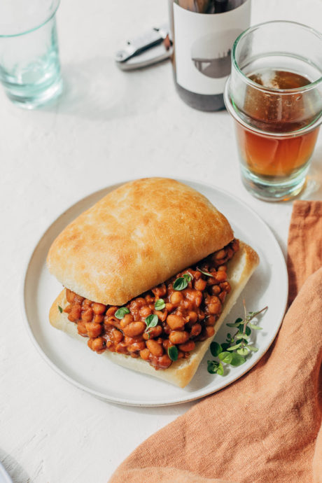 Close up of vegan baked beans served on a bun on a table with beer.
