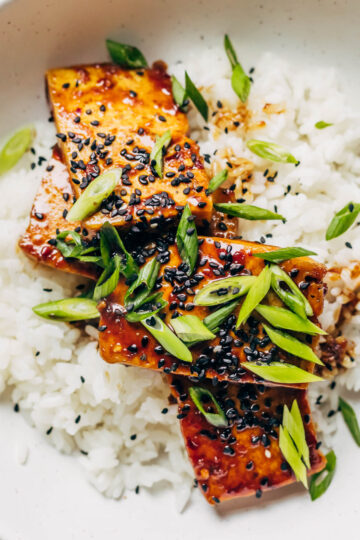 Close up pf sticky teriyaki on white rice with green onions and black sesame seeds.