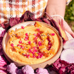 Woman holding a tray of vegetables with a bowl of orange dip.