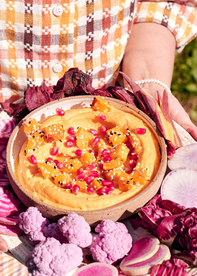 Woman holding a tray of vegetables with a bowl of orange dip.