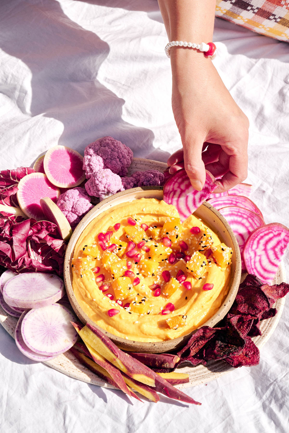 A bowl of butternut squash harissa dip alongside pretty purple veggies.