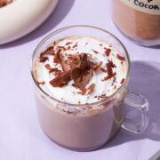 A glass mug of hot chocolate topped with cream and chocolate shavings.
