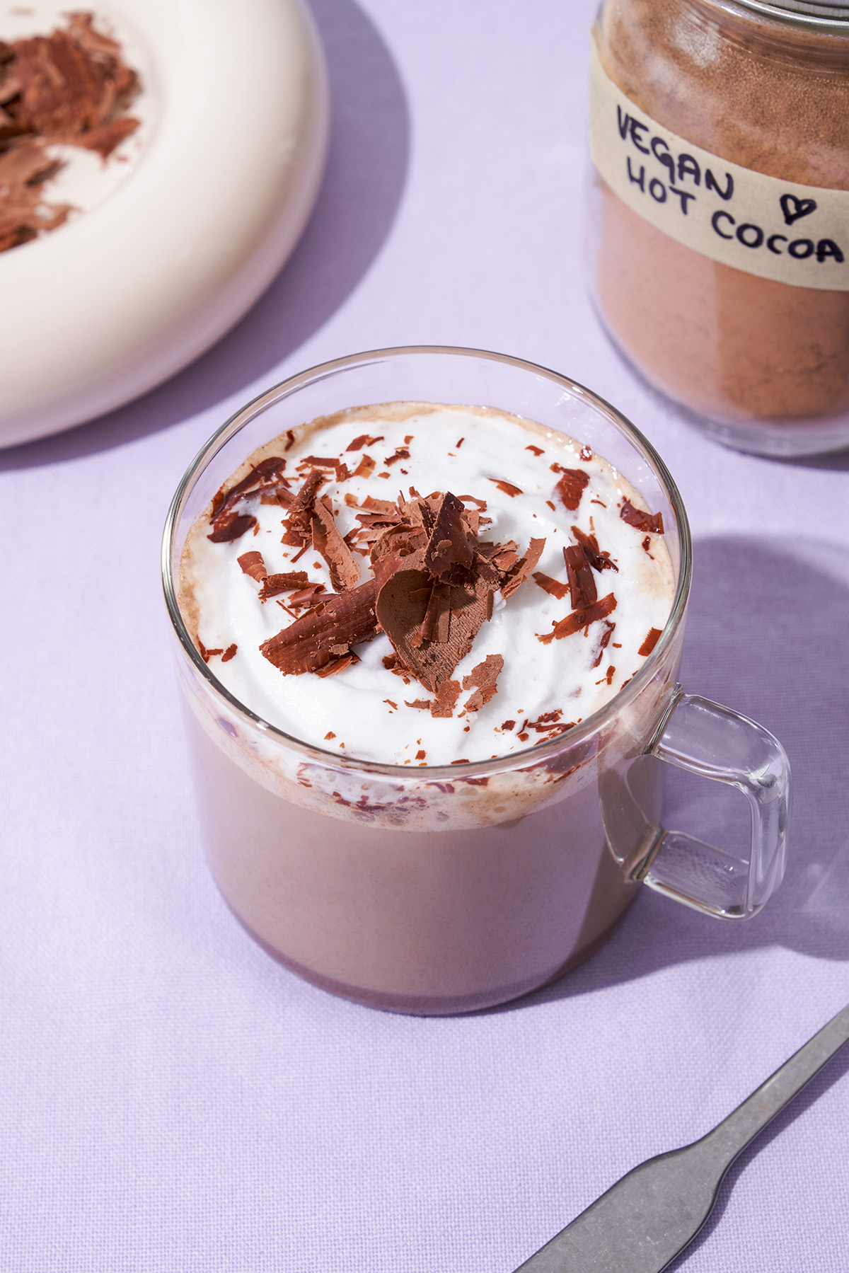 A glass mug of hot chocolate topped with cream and chocolate shavings.