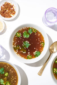 Vegetable broth in a bowl with sesame seeds and cilantro.