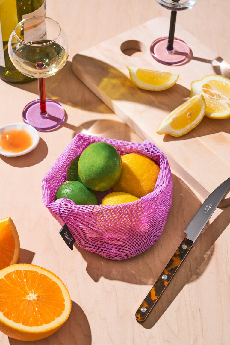 Oranges and limes in a produce bag with more citrus around.