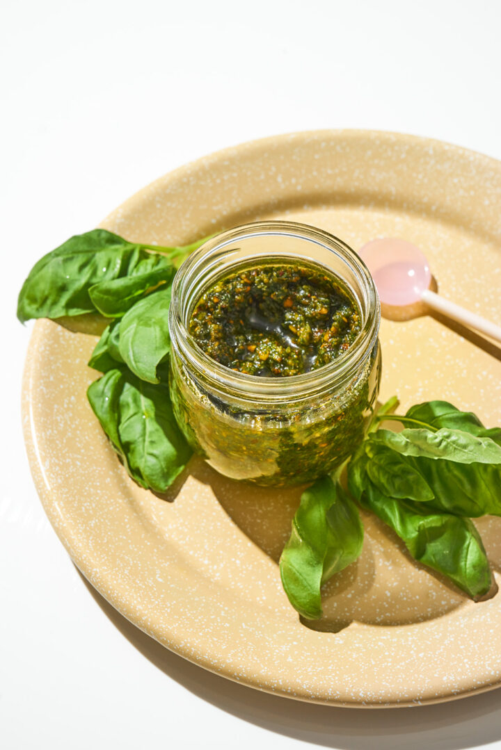 A jar of pesto on a plate with basil leaves around.