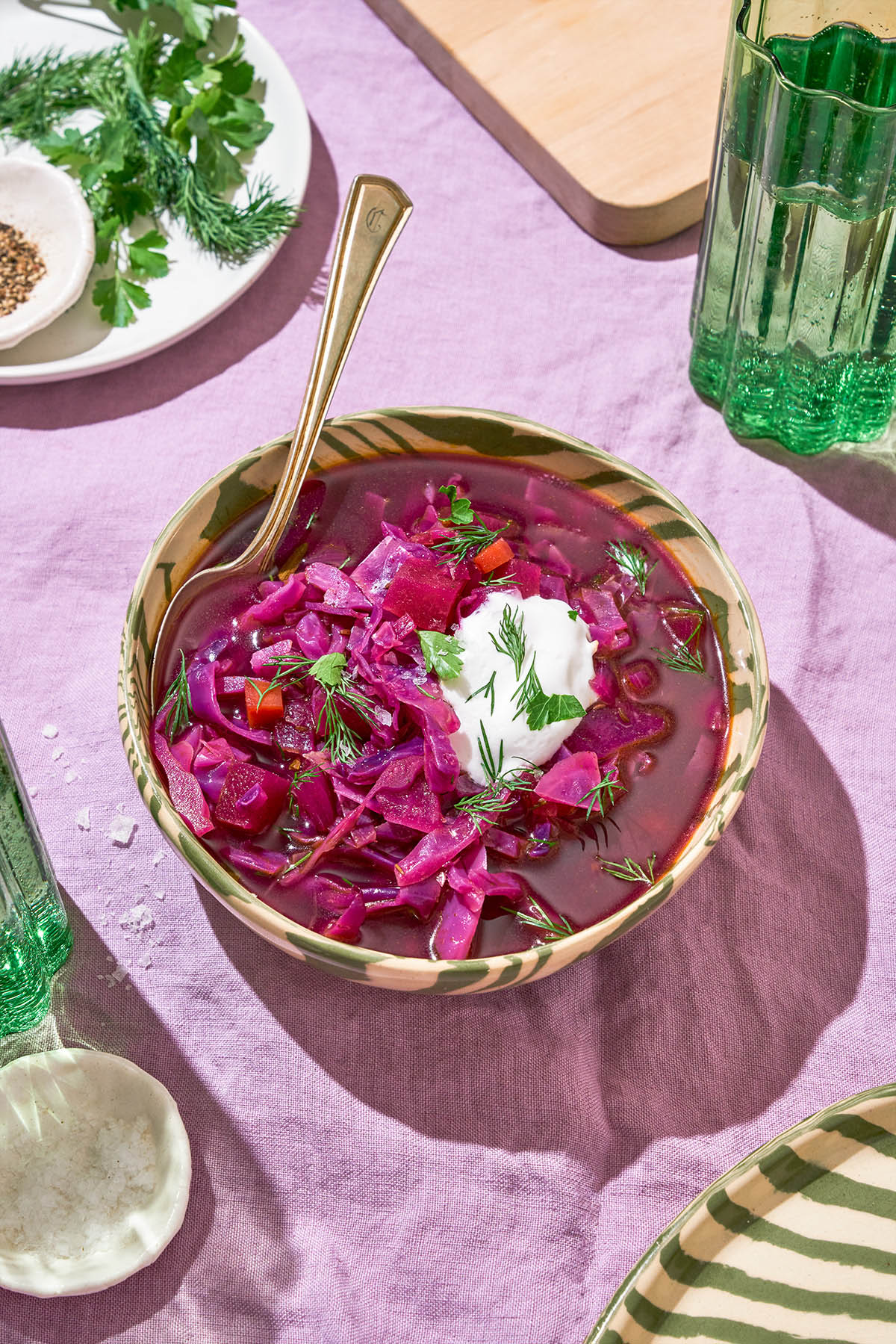 A bowl of purple cabbage soup topped with sour cream and herbs.