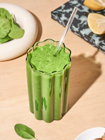 A wavy glass filled with a green smoothie, topped with a glass straw.