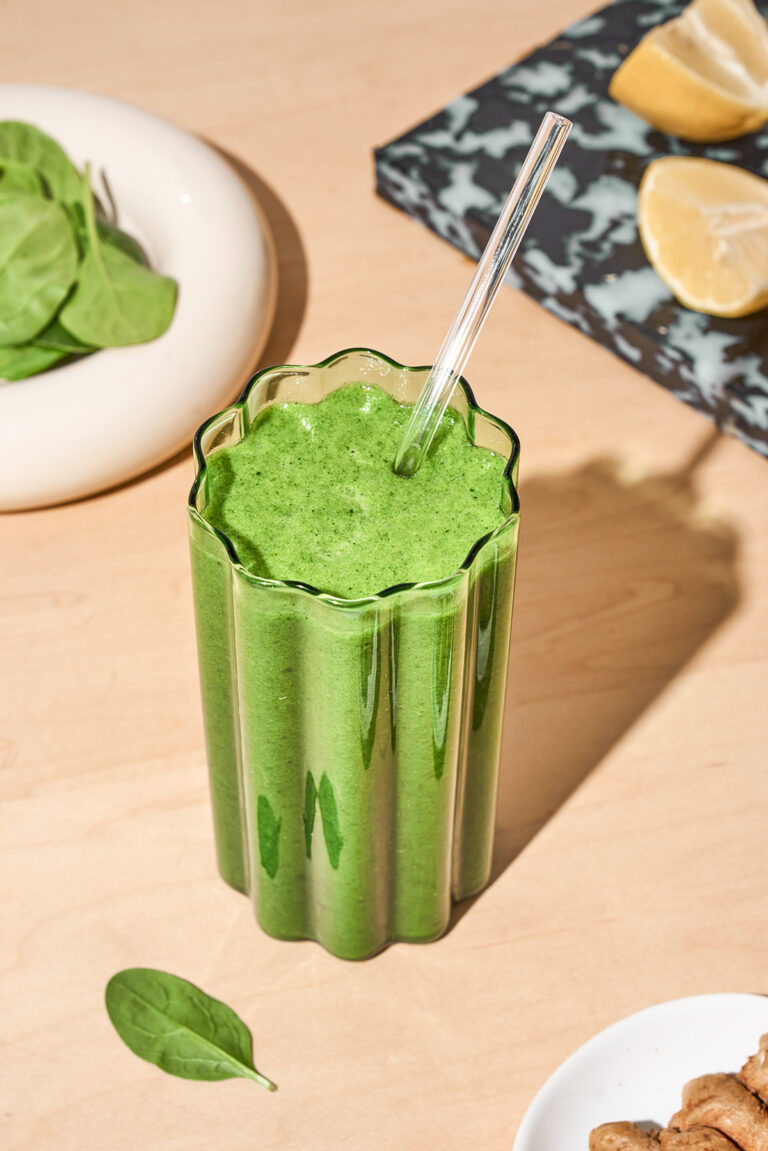 A wavy glass filled with a green smoothie, topped with a glass straw.