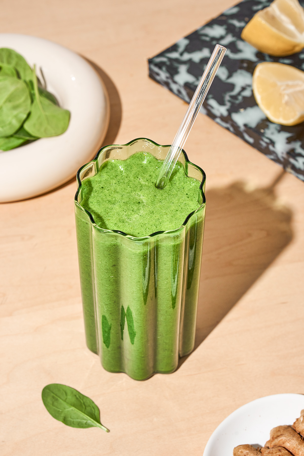 A wavy glass of green smoothie with a glass straw.