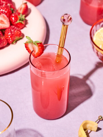 A brightly lit scene with a glass of pink juice and strawberries.