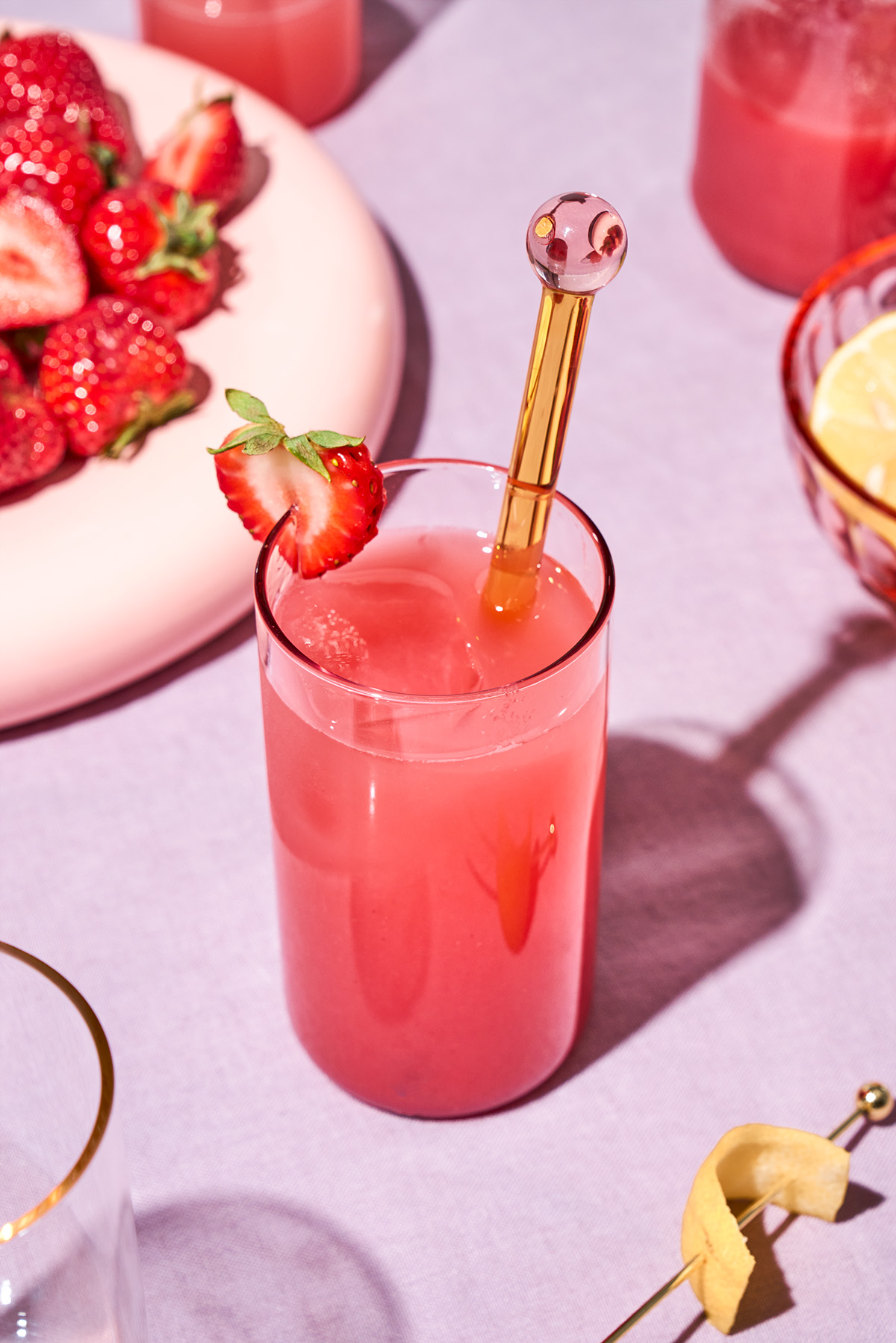 A brightly lit scene with a glass of pink juice and strawberries.
