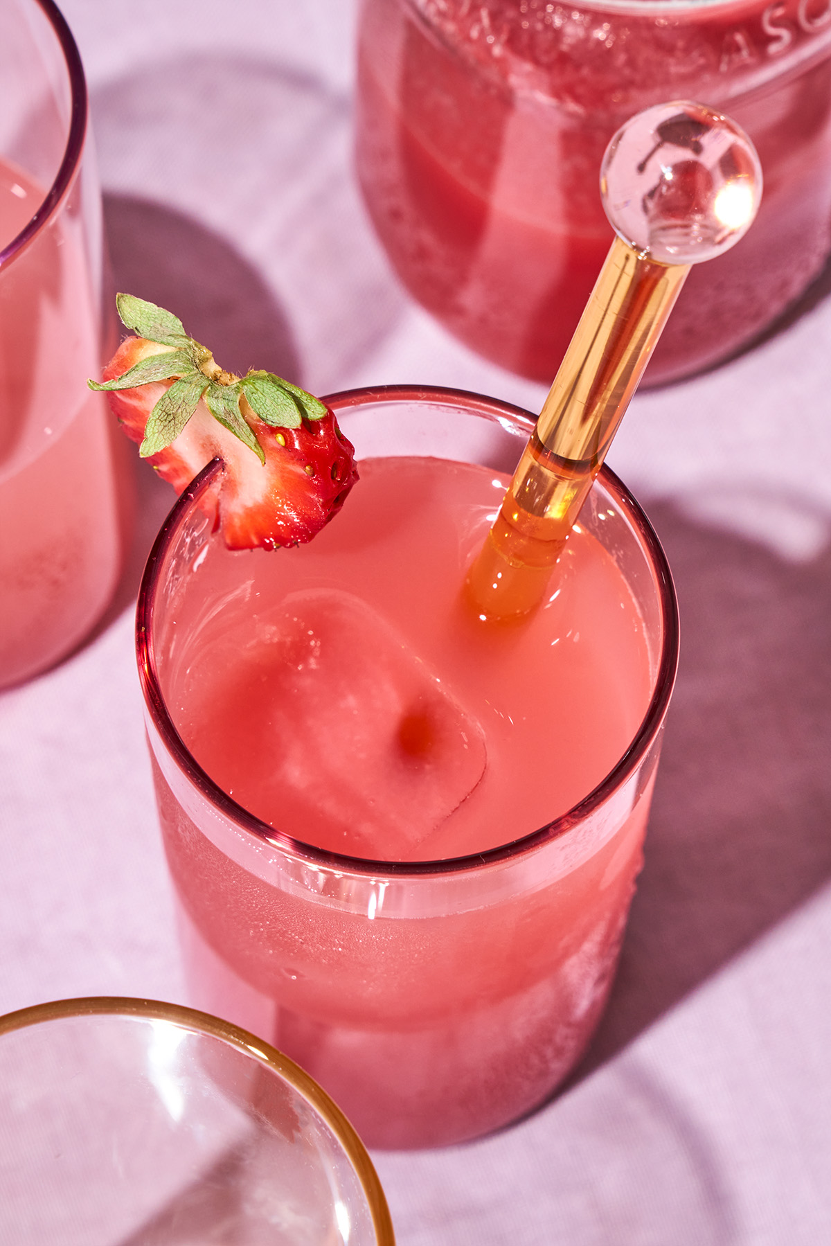 Close up of pink juice with ice in a glass with a strawberry.