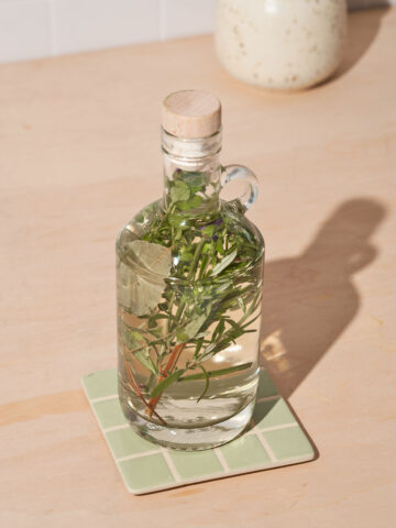 A glass bottle of vinegar with fresh herbs submerged in it.