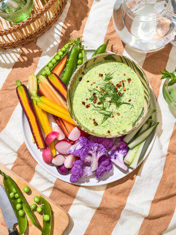 Bowl of green dip on a plate with raw vegetables at a picnic.