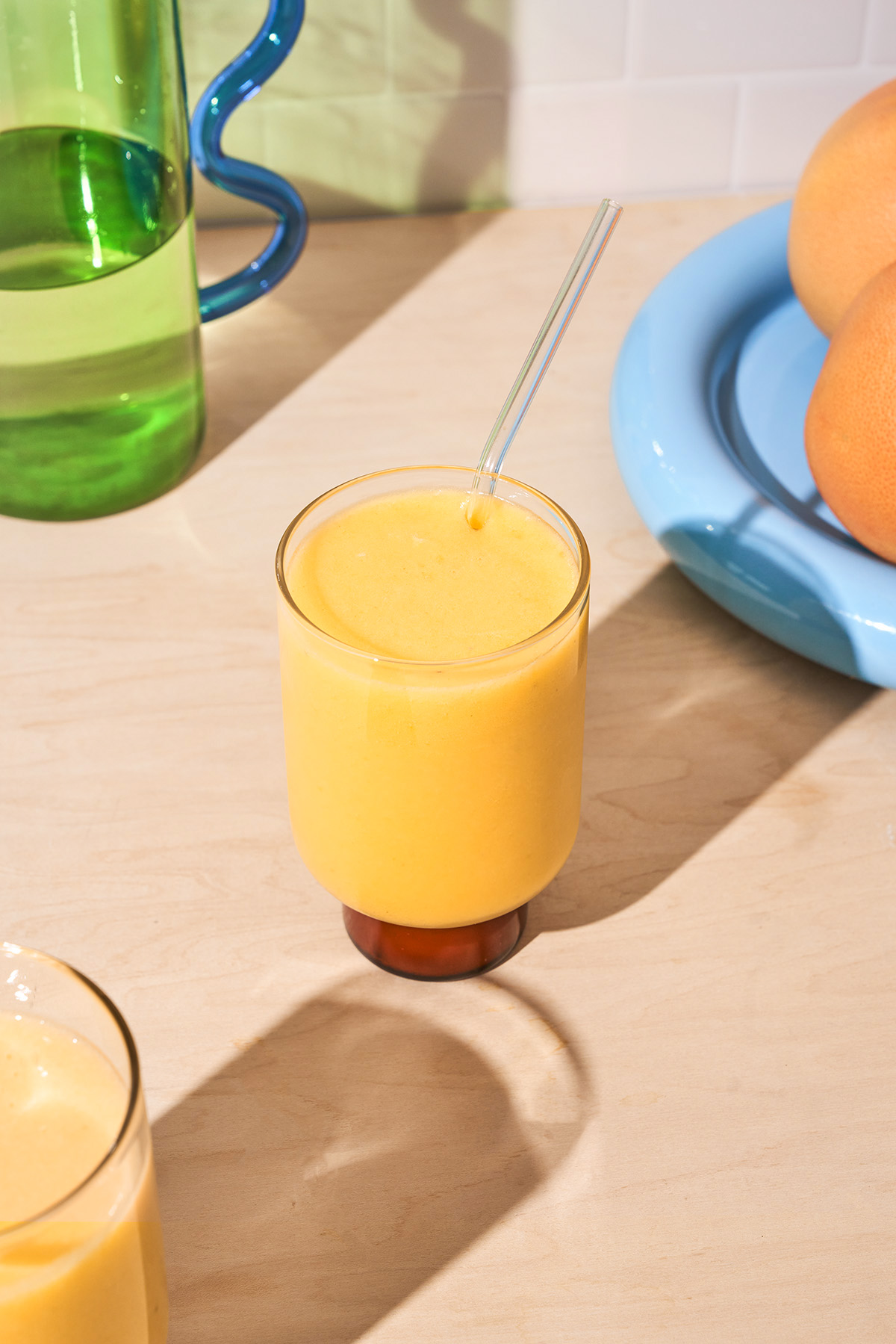 An orange smoothie in a glass with a glass straw on a kitchen countertop.