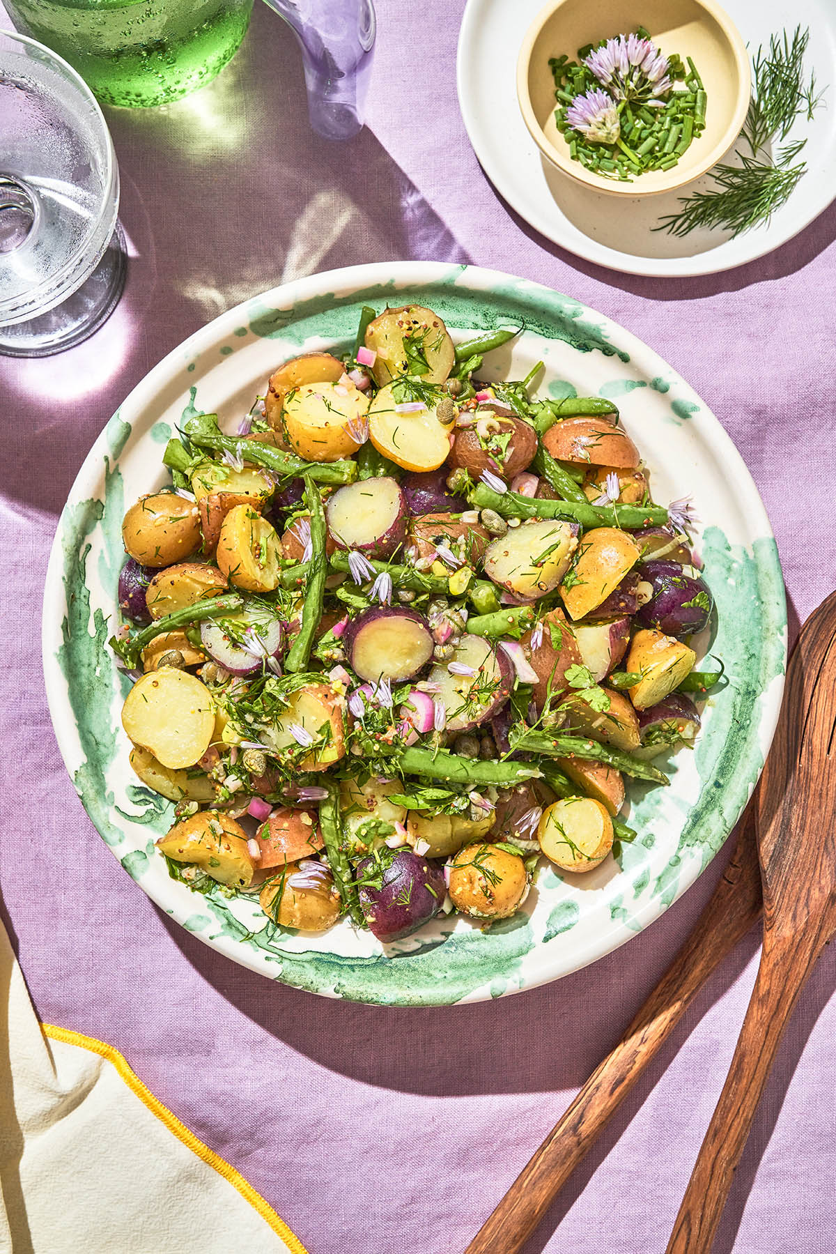 Potato salad with herbs and green beans in a big bowl on a picnic blanket.