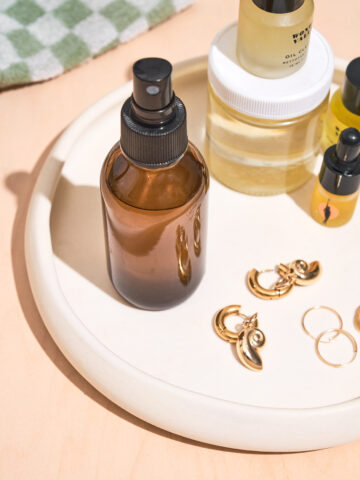 An amber glass spray bottle on a tray with oils and gold earrings.