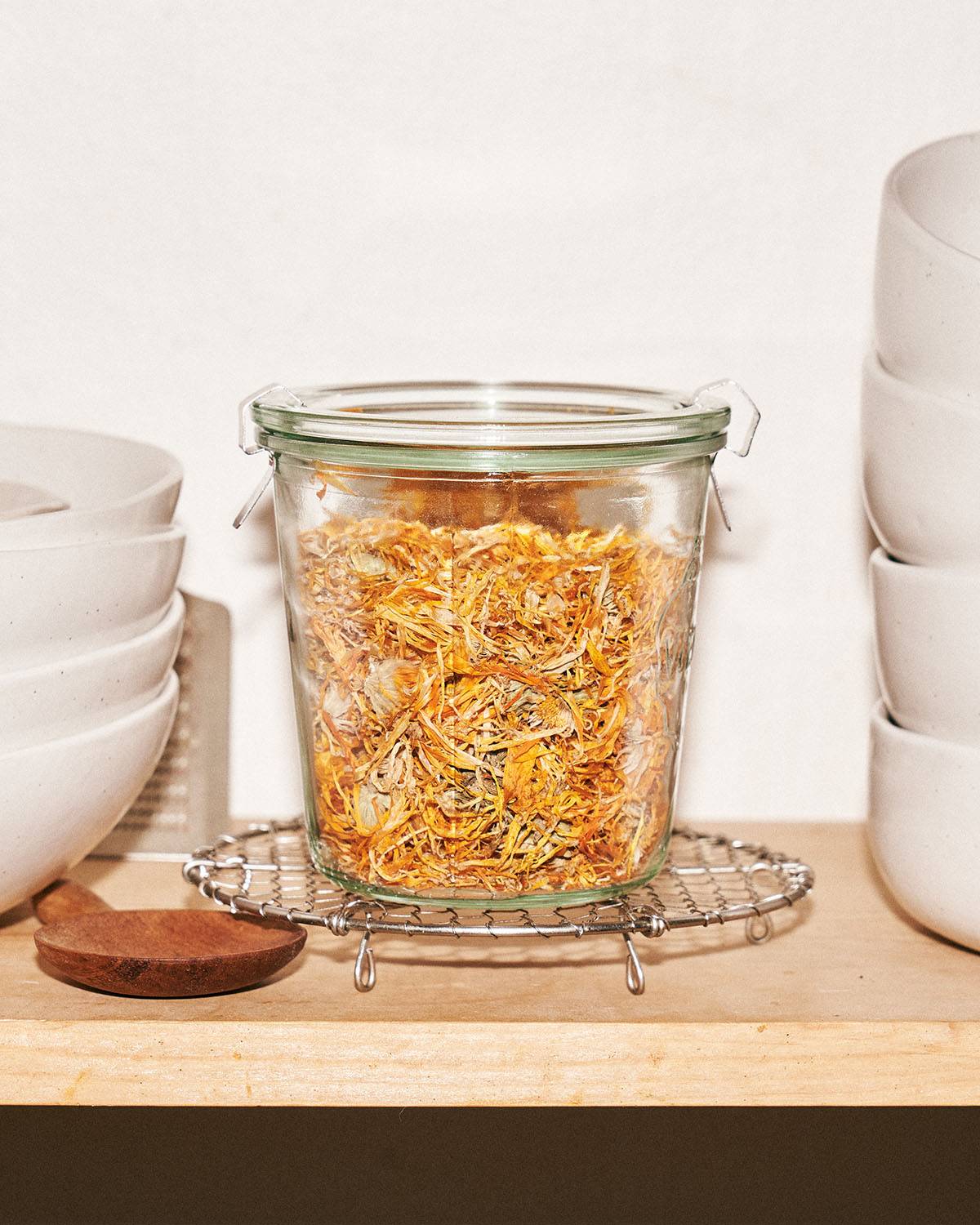 A Weck jar filled with dry calendula petals on a kitchen shelf.