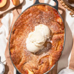 A peach cobbler in a picnic setting topped with scoops of vanilla ice cream.