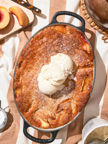 A peach cobbler in a picnic setting topped with scoops of vanilla ice cream.