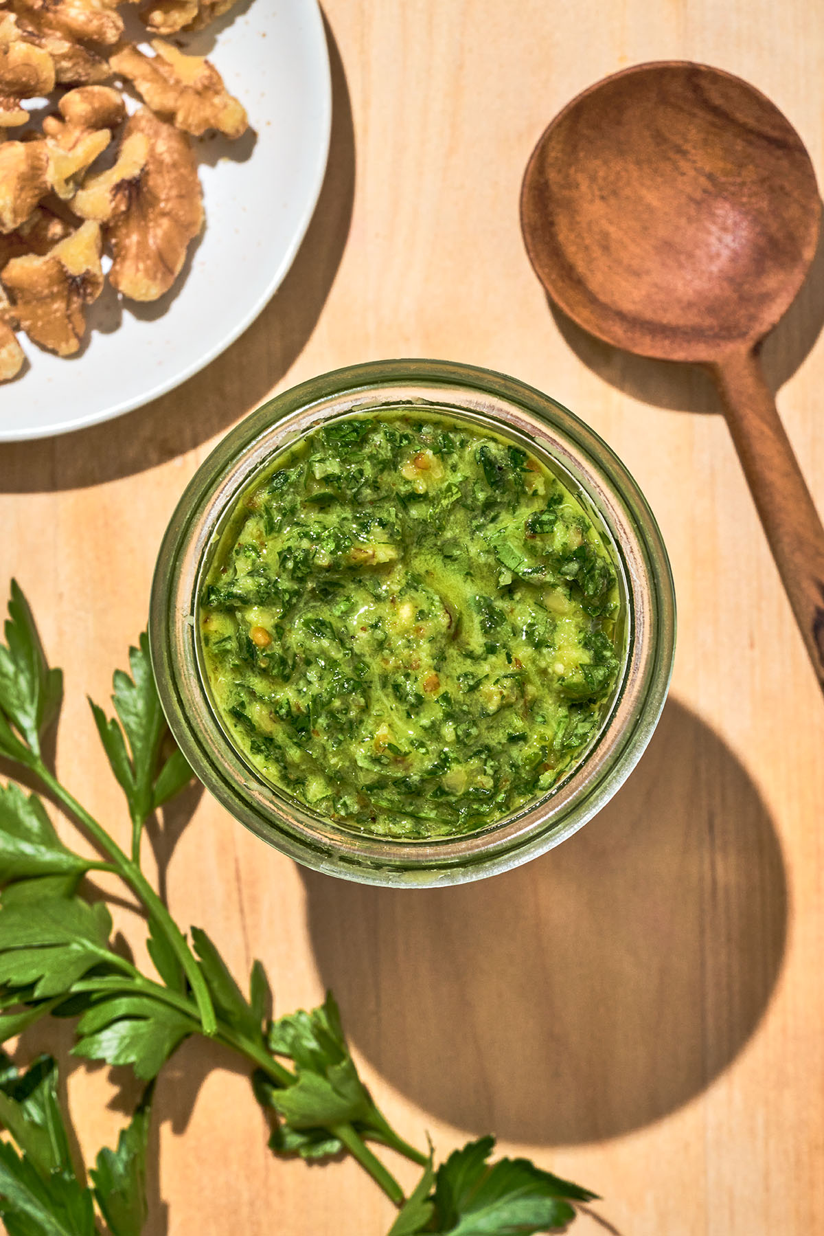 Top-down view of a jar of pesto with parsley and walnuts around.