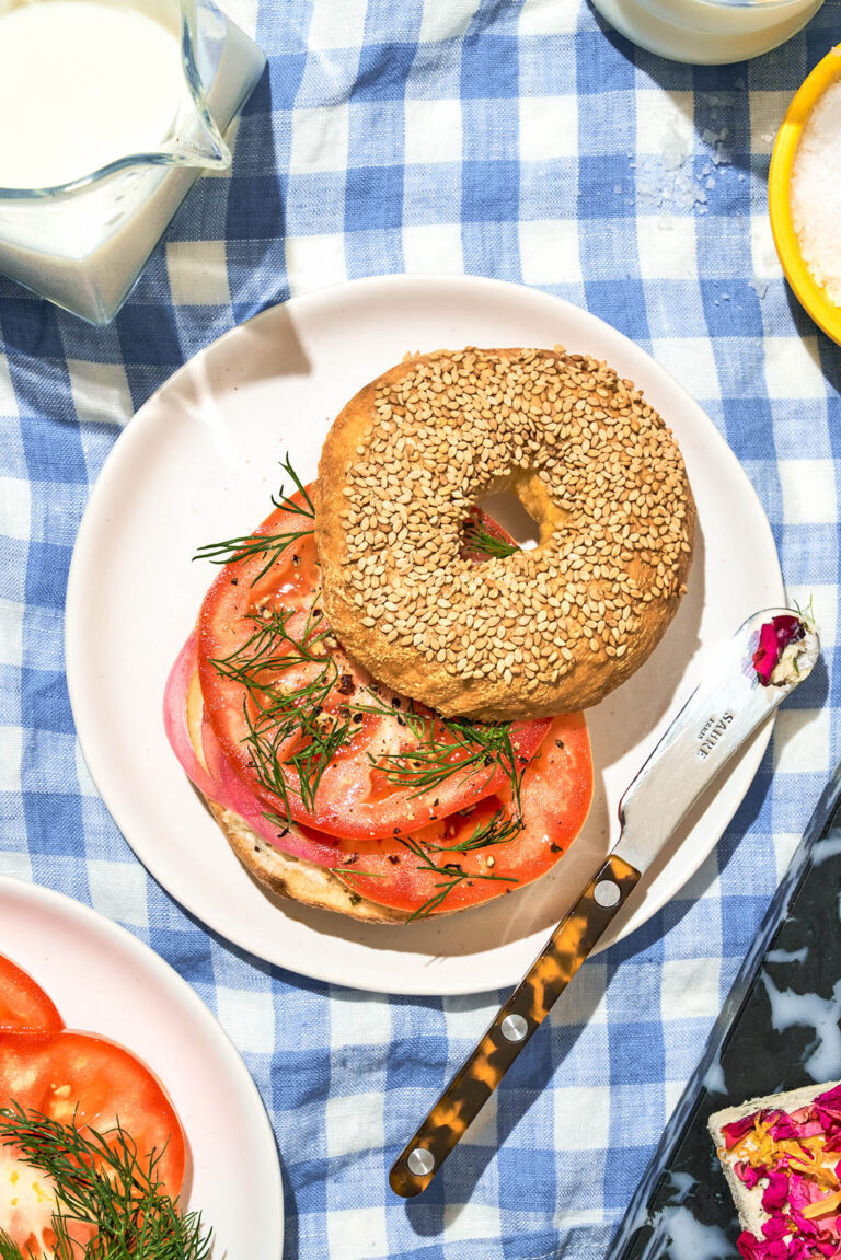 Top-down view of a sesame bagel sandwich on a picnic blanket.