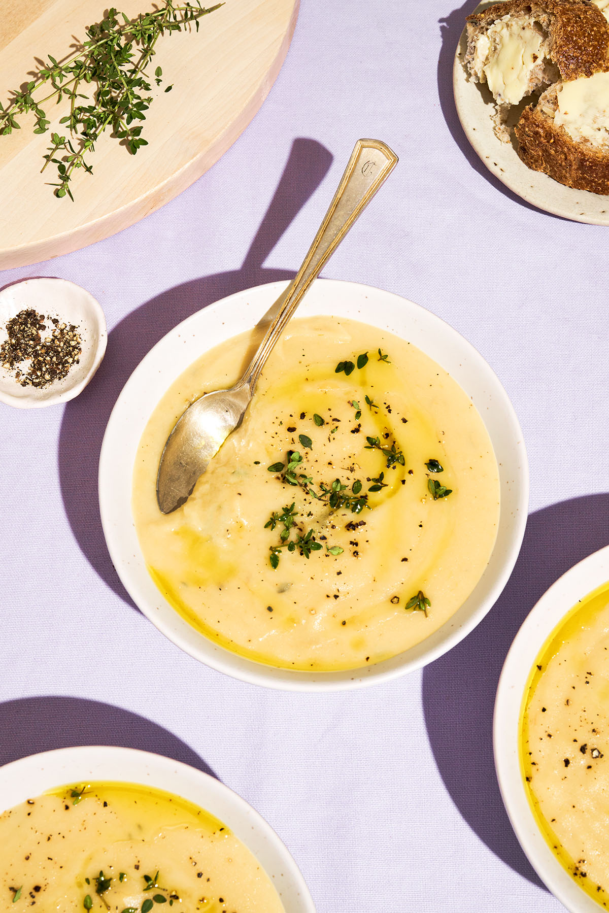 Brightly lit creamy leek soup in bowls topped with herbs.