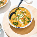 A bowl of lentil soup topped with herbs and cheese in strong light.