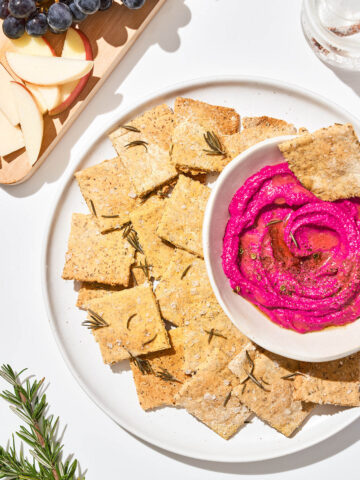 Crackers on a large plate with beetroot dip and fruit beside.