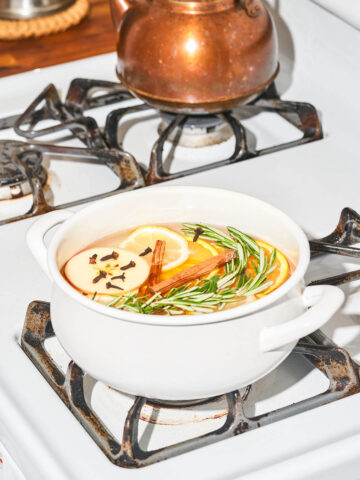 Fruit, herbs, and spices in a white pot on a gas stovetop.