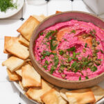Beet root hummus in a bowl with crackers on a plate.