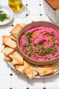 Beet root hummus in a bowl with crackers on a plate.