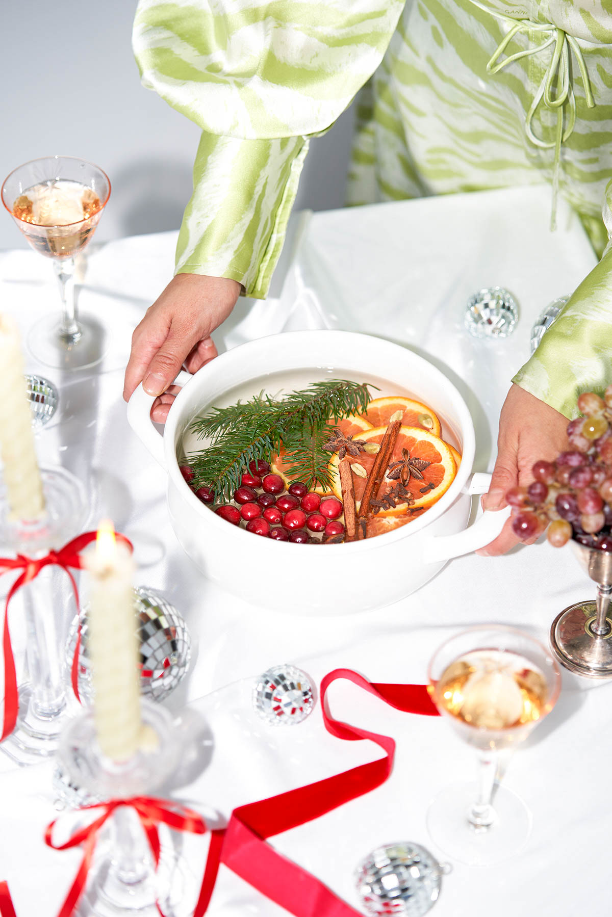 A holiday table setting with a woman holding a pot filled with fruits and spices.