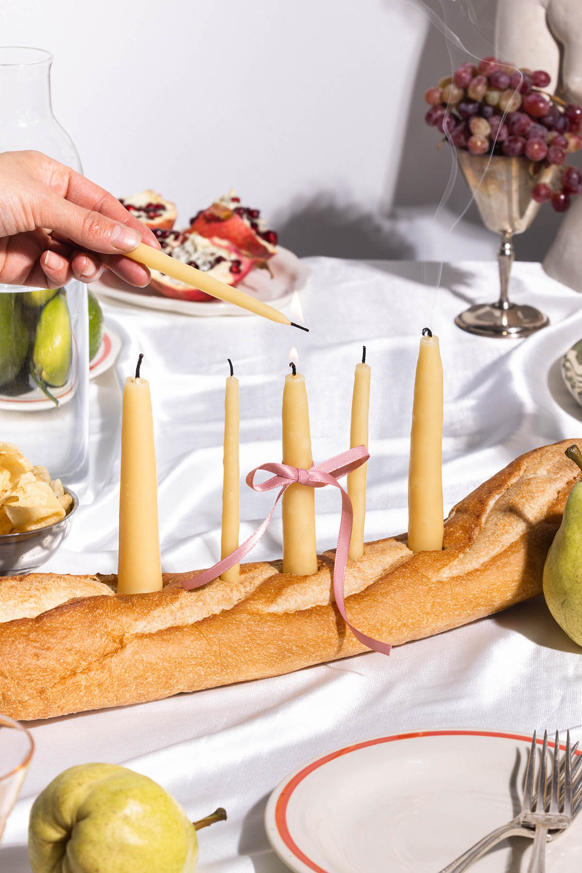 Using a candle to light another candle, beeswax tapers using a baguette as a holder.