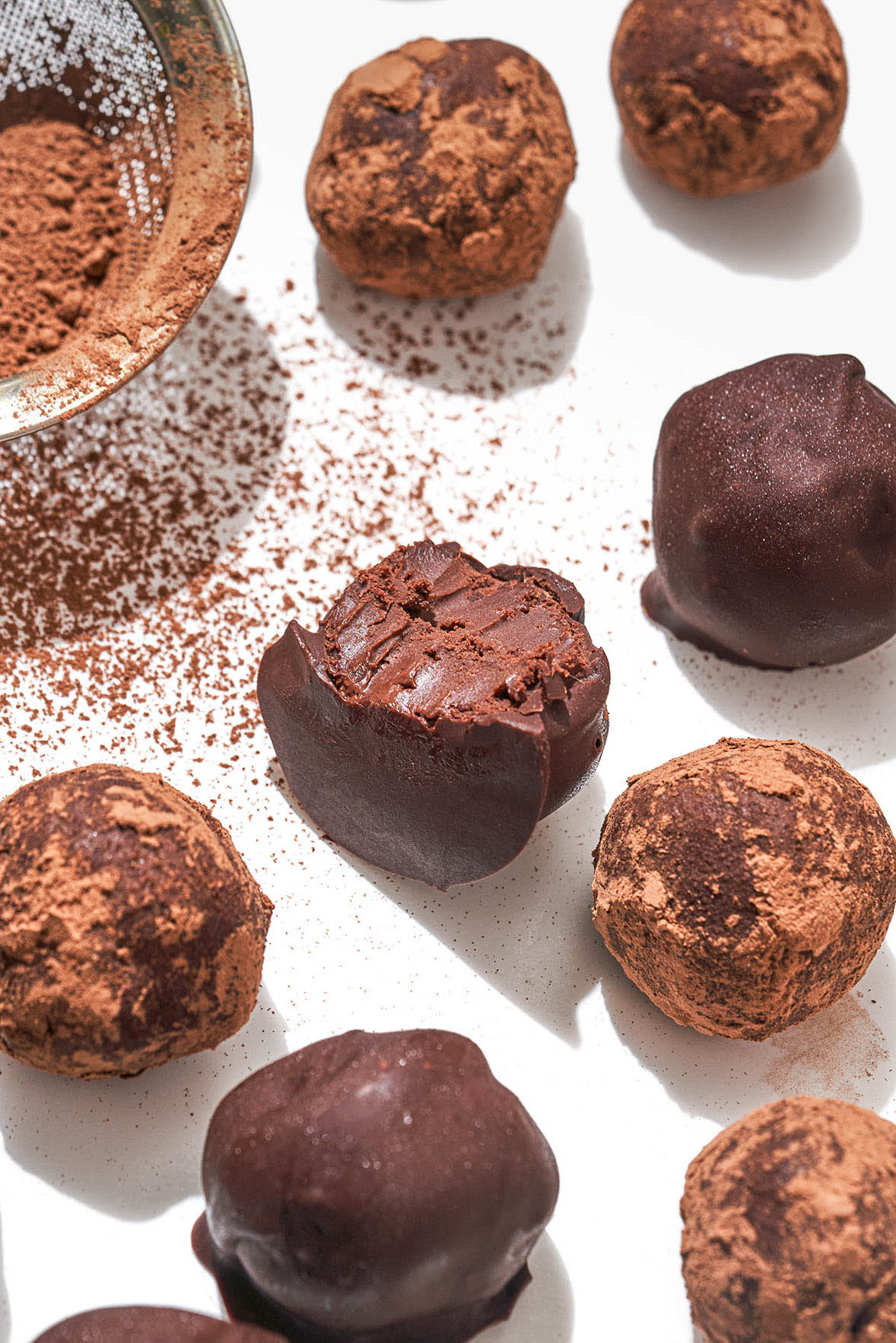 Several cocoa and chocolate coated truffles on a white surface.