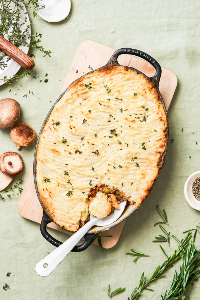 Top down view of potato-topped pie with a serving spoon in the dish.