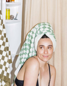 Woman in a washroom setting with a towel wrapped around her head.