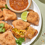 Baked samosas on a plate with dip in a small bowl.