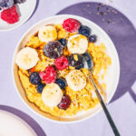 Yellow porridge in a bowl topped with berries and banana.