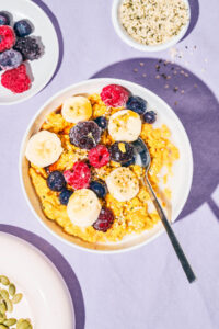 Yellow porridge in a bowl topped with berries and banana.
